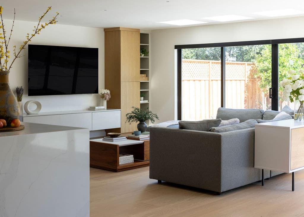 Open-plan living room remodel by Barcci Builders — oak built-ins, marble waterfall island, sliding glass doors to garden